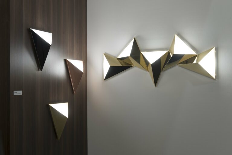 <p></noscript>The Tetra wall lamp comes in the form of a four-sided triangular module. Three sides are in solid brass, the fourth, in polycarbonate, which diffuses warm light from the integrated LED. With a contemporary and minimalist design, Tetra, placed on its own, will very easily adorn the walls of a hotel room, or in corridors, in repetition. In a bedroom or living room, it can easily be placed on either side of a mirror, on the headboard of the bed or a sofa.</p>
<p>In composition, the Tetra module will draw all your inspirations with light. Positioned side by side, the Tetra fixtures can be interconnected using a cable running between the wall and the back of the wall lamp. This assembly only requires a single electrical outlet. Whatever the type of space in which it fits, Tetra diffuses a delicate and harmonious variable light (phase-cut variation). The triangular luminaire is available in all the finishes offered by CVL: brass, graphite, nickel and copper, in a satin or polished decor. By multiplying and organizing several lights, assembled, they quickly become a decorative object with a unique visual effect !</p>
